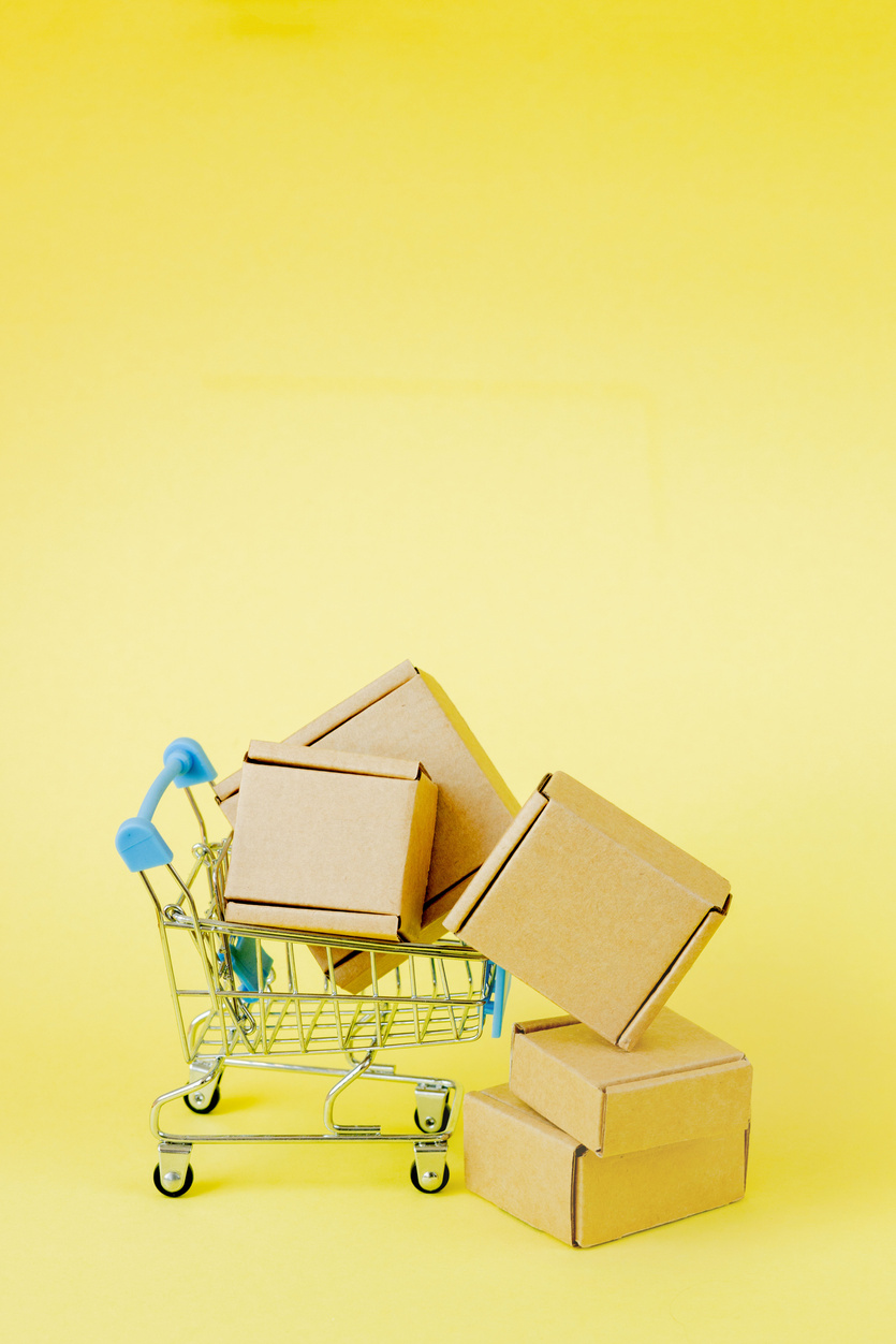 Paper shopping bags in a shopping cart on yellow background,